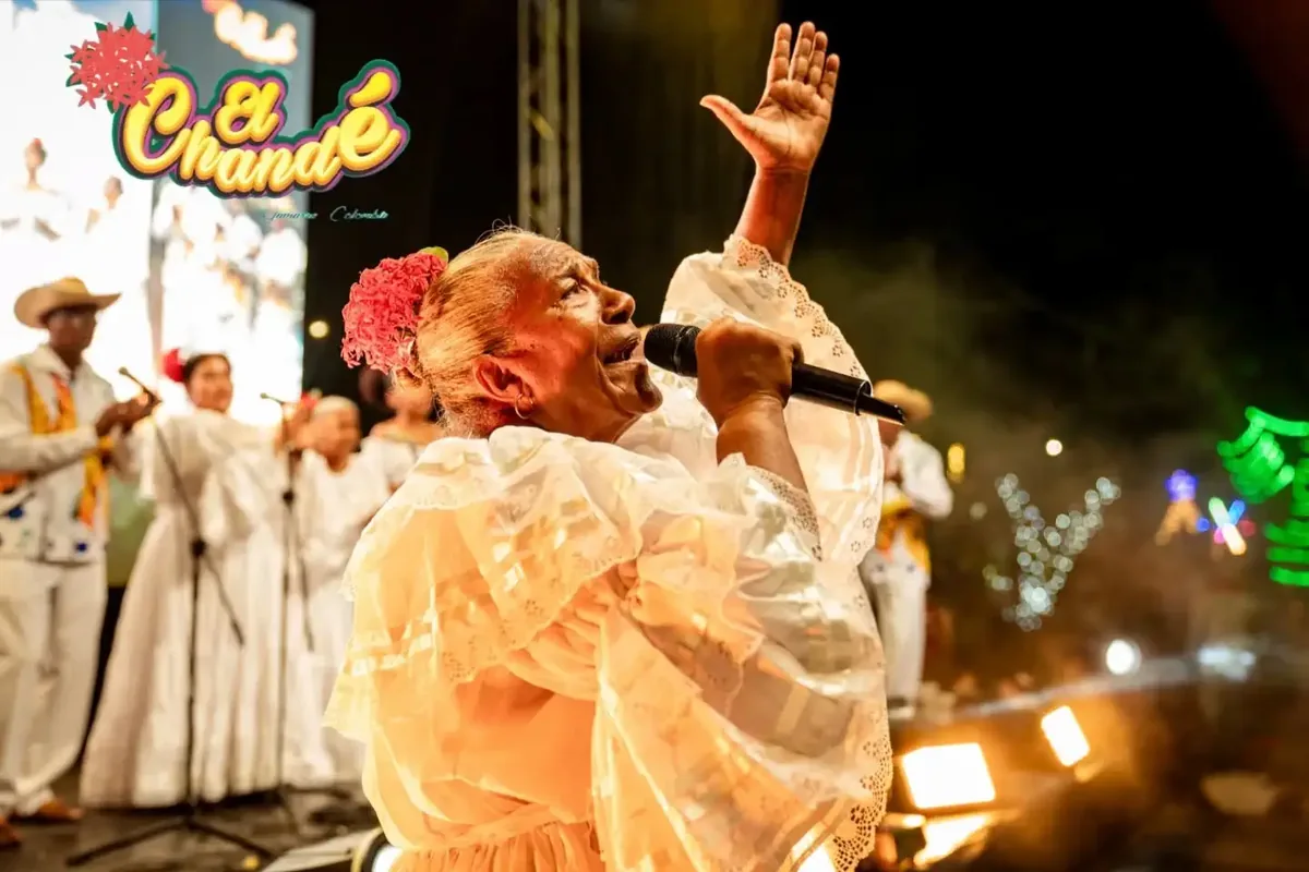 Adultos mayores con trajes blancos danzando a la luz de las velas en una plaza.