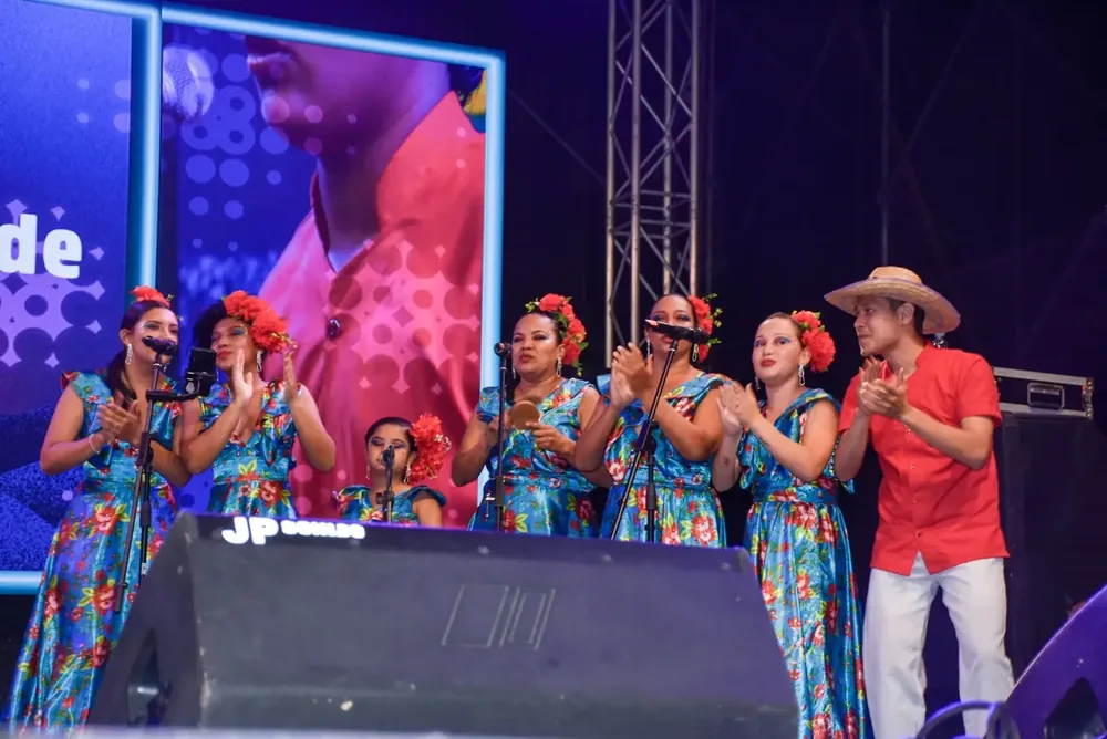 Grupo de cantadoras y músicos aplaudiendo en tarima durante una presentación en vivo.