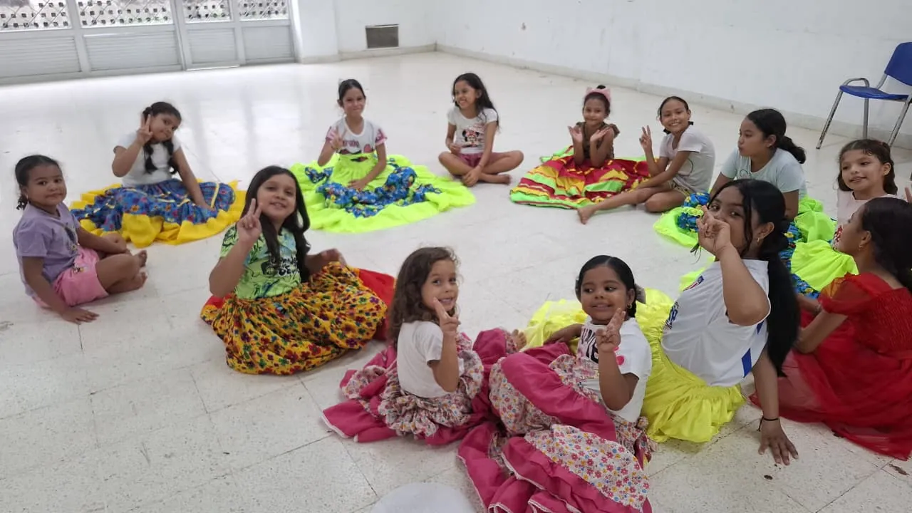 Niñas y niños con faldas de colores sentados en el suelo durante un taller de Gamarra vive su arte.